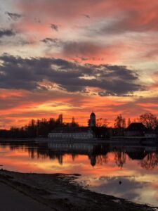 Ein rot-orangener Sonnenuntergang am Rhein beim Schänzle Konstanz. Der Sonnenuntergang spiegelt sich auf dem stillen Wasser im Rhein.