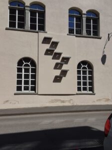 Blick auf die Südwand des Bürgersaals. Die verschobene Anordnung der Stahltableaus lässt mit ein wenig Fantasie die Buchstaben aufleuchten, stark verzerrt durch die Position der Sonne.
