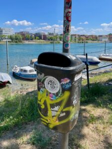 Sticker, Tags und kleine künstlerische Spuren an einem Mülleimer in Konstanz.