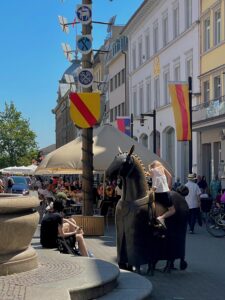 Kind sitzt auf der Pferdeskulptur neben dem Brunnen auf der Marktstätte.